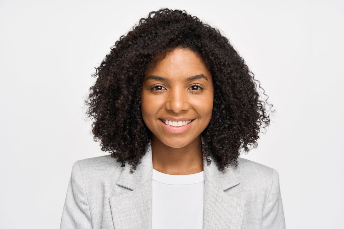 Happy confident young African American business woman standing isolated on white wall